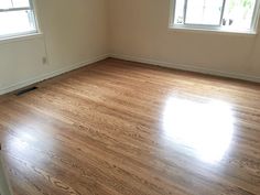 an empty room with hard wood floors and two windows