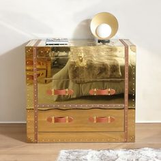 a mirrored chest with two drawers and gold trimmings on the bottom, in front of a white wall