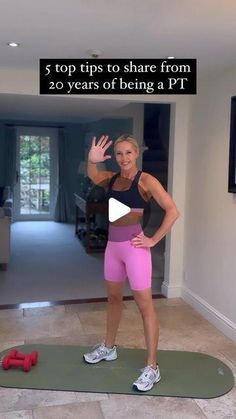 a woman in pink shorts and black top standing on a mat with her hands up