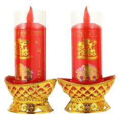 two red candles sitting next to each other on top of a gold plated stand