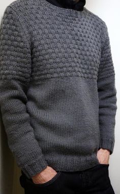 a man standing next to a white wall wearing a gray sweater and black turtle neck sweater