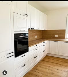 an empty kitchen with white cabinets and wood flooring on the counter top, along with black appliances