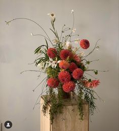 a wooden box with flowers and greenery in it sitting on a table next to a wall