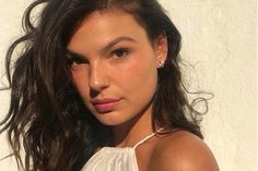 a close up of a person wearing a white shirt and posing for the camera with her hair blowing in the wind