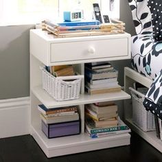 a white nightstand with books and magazines on it