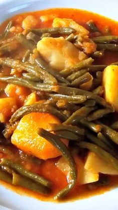 a white plate topped with green beans and carrots next to meat in gravy