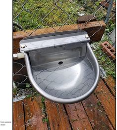 a metal toilet sitting on top of a wooden floor next to a chain link fence