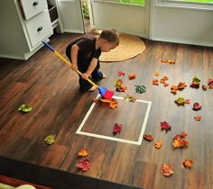 a young boy is playing with leaves on the floor in his living room while holding a broom