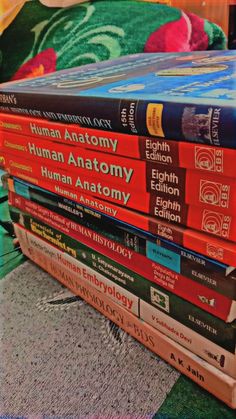 a stack of books sitting on top of a green chair next to a red pillow