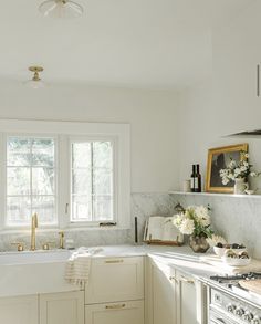 a kitchen with white cabinets and marble counter tops, gold faucet handles, an open window above the sink