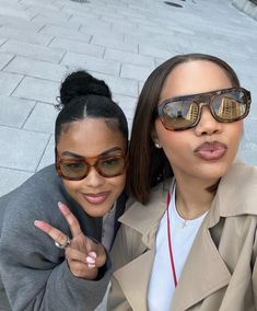 two women taking a selfie in front of a brick wall with their fingers up