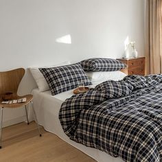 a bed with plaid sheets and pillows in a bedroom next to a wooden chair on the floor