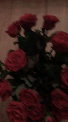 a vase filled with red roses sitting on top of a wooden table next to a wall