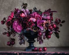 a vase filled with lots of purple flowers and red berries on top of a table