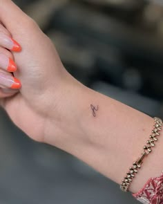 a woman's arm with a small tattoo on it and an orange manicure