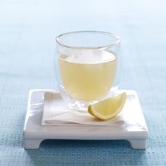 a glass of lemonade with a slice of lemon on the side sitting on a coaster