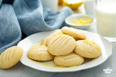 a white plate topped with lemon cookies next to a glass of milk and a blue towel