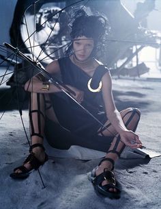 a woman sitting on the ground with an umbrella in her hand and wearing gladia sandals