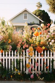 a white picket fence surrounded by flowers in front of a house