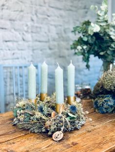 a wooden table topped with lots of candles next to a vase filled with greenery