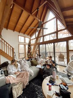 three people sitting on a couch in a living room with large windows and a christmas tree