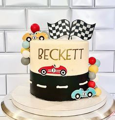 a birthday cake decorated with cars and flags on a silver platter in front of a white tile wall