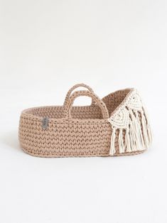 a crocheted basket with a handle and tassels on the bottom, sitting against a white background