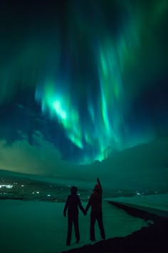 two people holding hands in front of an aurora bore over the ocean at night time