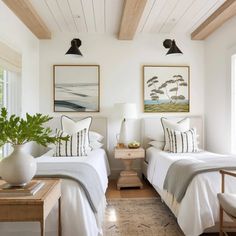 two beds in a room with white walls and wood beams on the ceiling, along with paintings above them