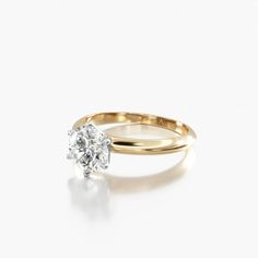 a yellow gold engagement ring with a single diamond in the center, on a white background