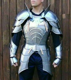 a man dressed in armor standing next to a wooden fence with his hands on his hips