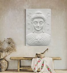 a white buddha statue sitting on top of a wooden bench next to a vase filled with flowers