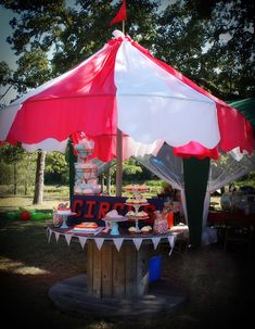 a table topped with lots of cupcakes under a red and white umbrella