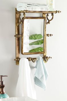 a bathroom mirror hanging on the wall above a sink and towel rack with folded towels