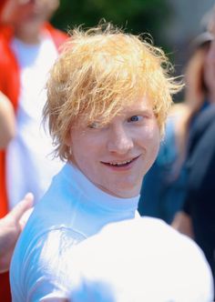 a young man with blonde hair and blue eyes smiles at the camera while standing in front of other people