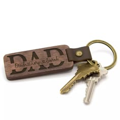 a wooden keychain with the word dad engraved on it and two keys attached to it