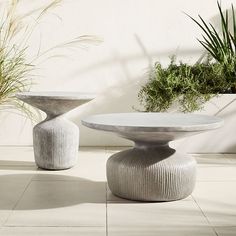 two white vases sitting next to each other on top of a tile floor near plants