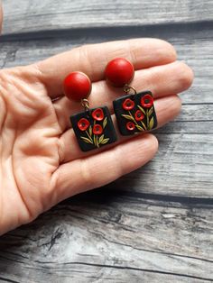 a pair of red and black square earrings with flowers on the front are held in someone's hand