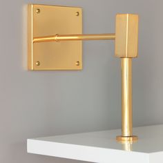 a white shelf topped with a gold colored wall mounted light and a metal hook on it