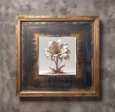 a gold frame with a white flower in it on a gray wall next to a painting