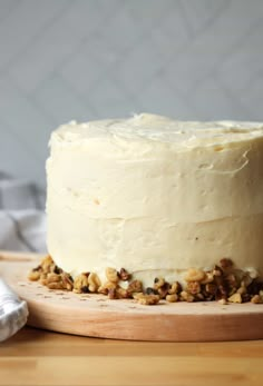 a cake with white frosting and walnuts on a wooden board next to a napkin