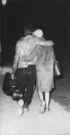 a man and woman walking down the street at night with their arms around each other