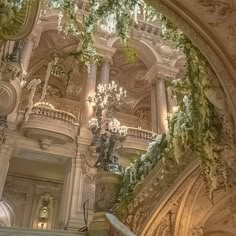 an ornate staircase with chandeliers and greenery on the ceiling in a building