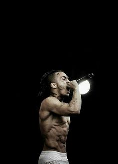 a shirtless man with no shirt on holding a microphone in his right hand and looking up at the sky