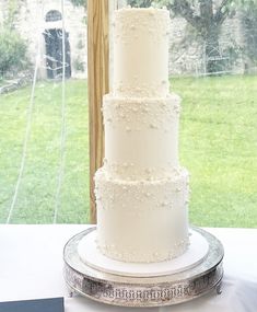 a three tiered white cake sitting on top of a silver platter next to a window