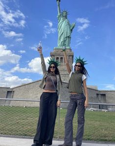 two women standing next to each other in front of the statue of liberty with their hands up