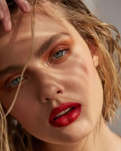 a woman with bright red lipstick on her face and hair blowing in the wind, looking at the camera