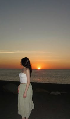 a woman standing in front of the ocean at sunset