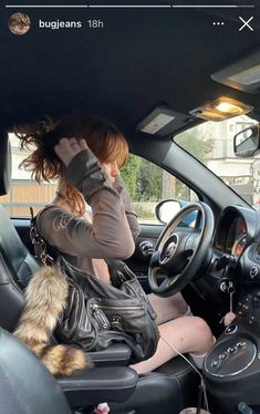 a woman sitting in the driver's seat of a car while holding her hand up to her head