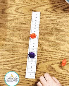 a child's hand is playing with the numbers on a wooden table next to orange and purple gummy bears